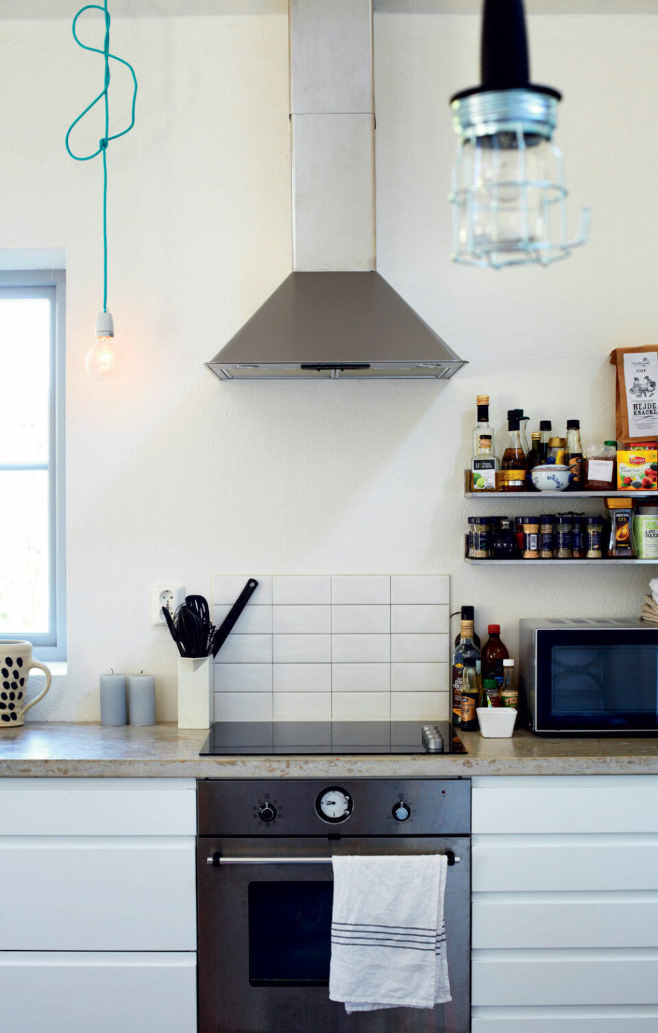Simple hylder rummer alle de lækre krydderier til madlavningen. Fliserne bag komfuret er en praktisk, enkel og prisvenlig løsning til at skåne væggen. Lamperne er lavet af et par porcelænsfatninger med turkise ledninger.