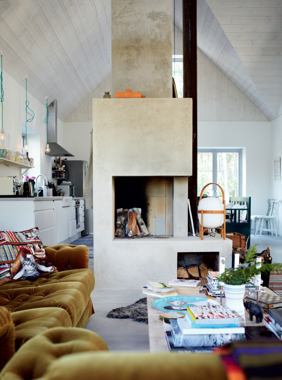 Køkkenalrummet deles smukt op med en pejs, som bliver flittigt brugt om vinteren. Sofabordet er hjemmelavet af birketræsplanker med mursten under som ben. De bløde sofaer stammer fra en vens sommerhus. Bordlampen Cesta fås herhjemme, bl.a. hos Casa Shop.