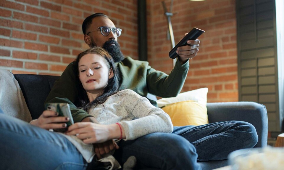 Par ser tv, mens kvinde kigger på sin mobiltelefon