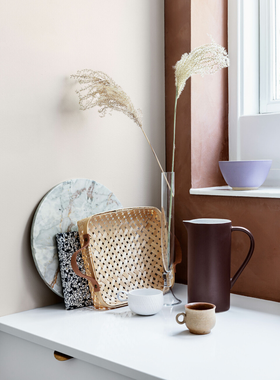 Terrazzopladen er fra OK design, kurven er fra Oyoy og den hvide kop er fra Robynn Storgaard. Den brune kande er fra H&M Home og det øvrige er fundet i genbrugsbutikker. Den lyse væg er malet med farven Summer Suede fra Dyrup og den terrakottafarvede er malet med mineral- kalkmaling fra Jotun Lady i farven Rustik Terrakotta.