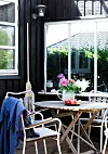 Langs den ene side af den overdækkede terrasse er der sat en væg op, så der er læ selv på en blæsende dag. Vinduet i væggen er købt på dba.dk. Havebordet er fra Ikea og Marguerit-stolene er klunset.