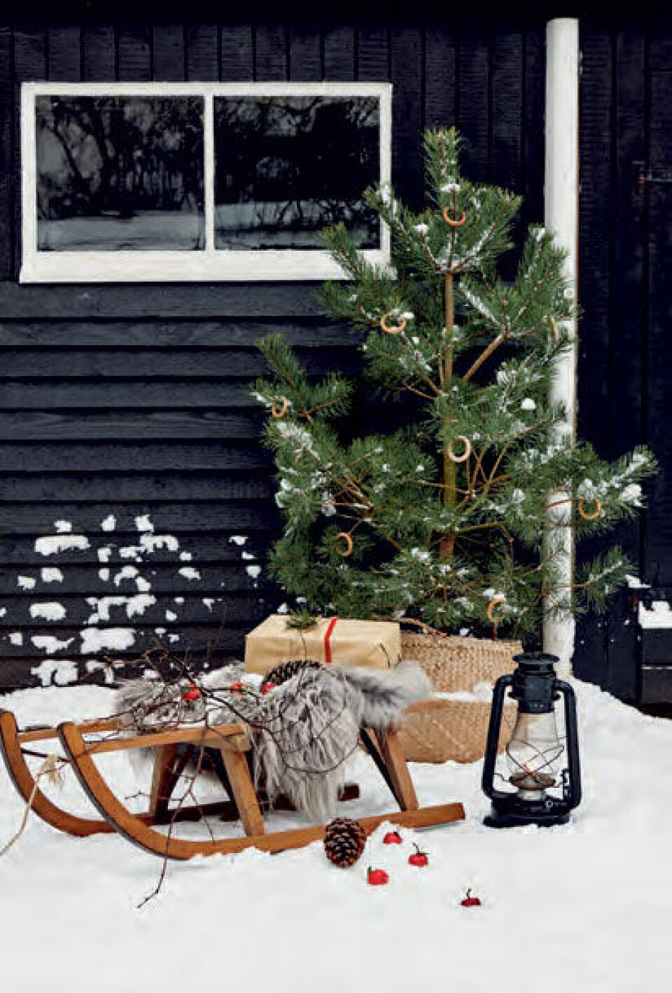 Kælken står fremme med fåreskind og grene fra haven, og petroleumslampen lyser op i sneen.