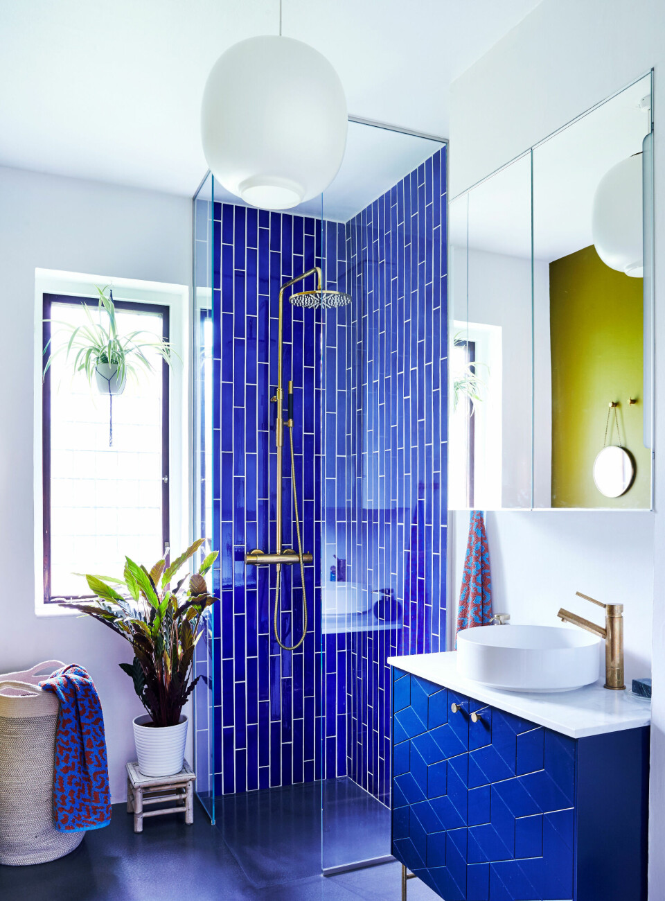 Badeværelset er parrets drømmebadeværelse og den seneste renovering i huset. Malingen er mosgrøn fra File under Pop, hvor de indigoblå fliser også er fra. Armaturerne er fra svenske Tapwell, og møblementet er fra Superfront. Vasketøjskurven og det runde spejl er fra H&M Home.