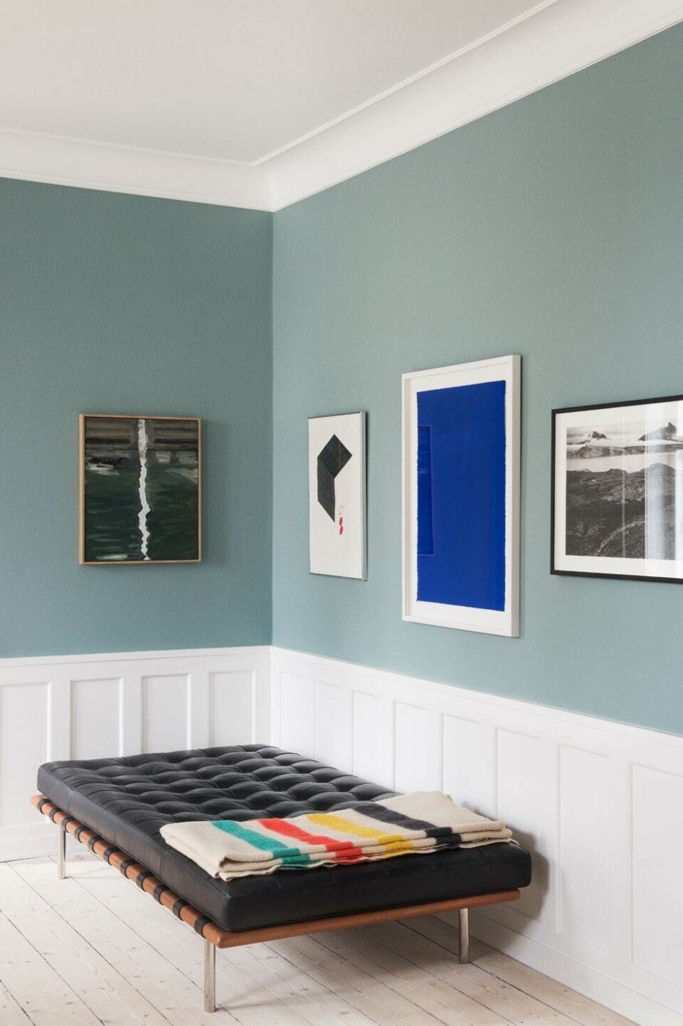 Væggen er malet med Oval room blue fra Farrow and Ball. Det grønne maleri er af Anne Berger, litografi af Schwalbe, det blå værk af Anders Bülow, og fotoet af Per Bak Jensen fik Trine i 30 års fødselsdagsgave af sine forældre. Daybed Barcelona er hjembragt fra New York, og plaiden er et loppefund. Foto: Gyrithe Lemche