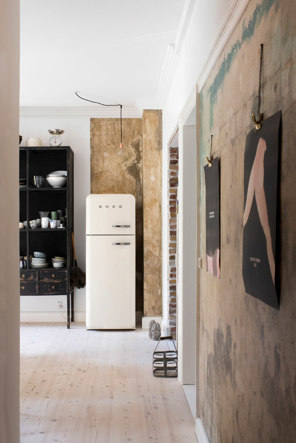 Væggen i gangen samt bag køleskabet har Clifford stået for. Han rev det gamle tapet ned for at sætte nyt op, men blev så glad for de rå vægge, at de fik lov at stå sådan. Plakaterne er købt på Charlottenborg kunstmuseum.