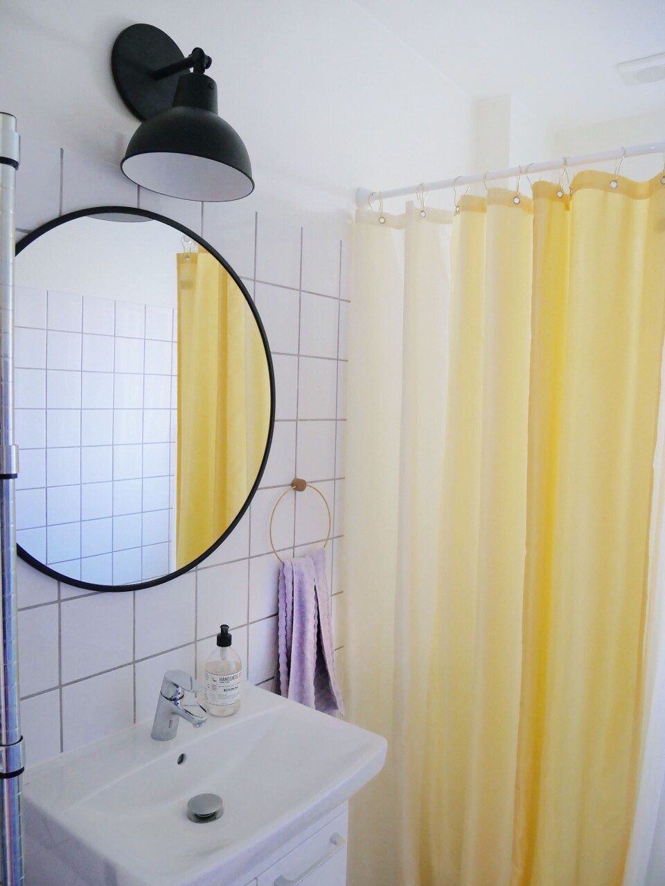 Det hvide badeværelse er piftet op med et gult badeforhæng fra HAY og et lilla håndklæde fra Ferm Living.