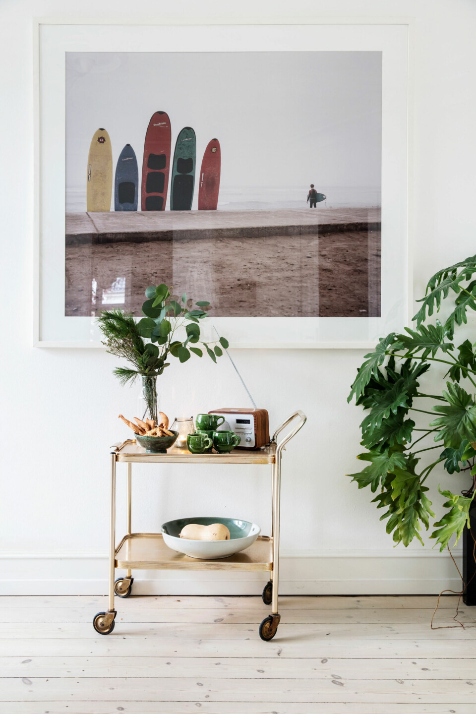 Store grønne planter skaber liv og binder rummets farver sammen. Det lille, gyldne barbord er et loppefund.