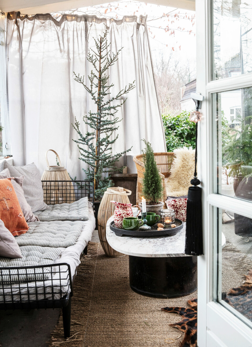 Den overdækkede terrasse er gjort klar til jul – med grantræer, lune tekstiler og lys i lygterne. Trådsofaen er et loppefund, marmorbordpladen er købt på DBA, og keramikken er fra Marokko.