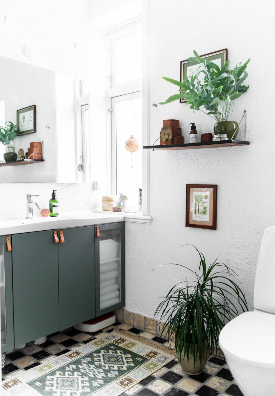 Da parret overtog lejligheden var badeværelset kedeligt og anonymt, men nu er fronterne blevet malet i en støvet grøn nunance, der er monteret hjemmelavede greb i læder og så har de fyldt rummet med loppefund og planter.