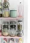 I køkkenet fortsætter pastelfarverne på de åbne hylder med klare beholdere, hvor æstetik og praktik går op i en højere enhed.