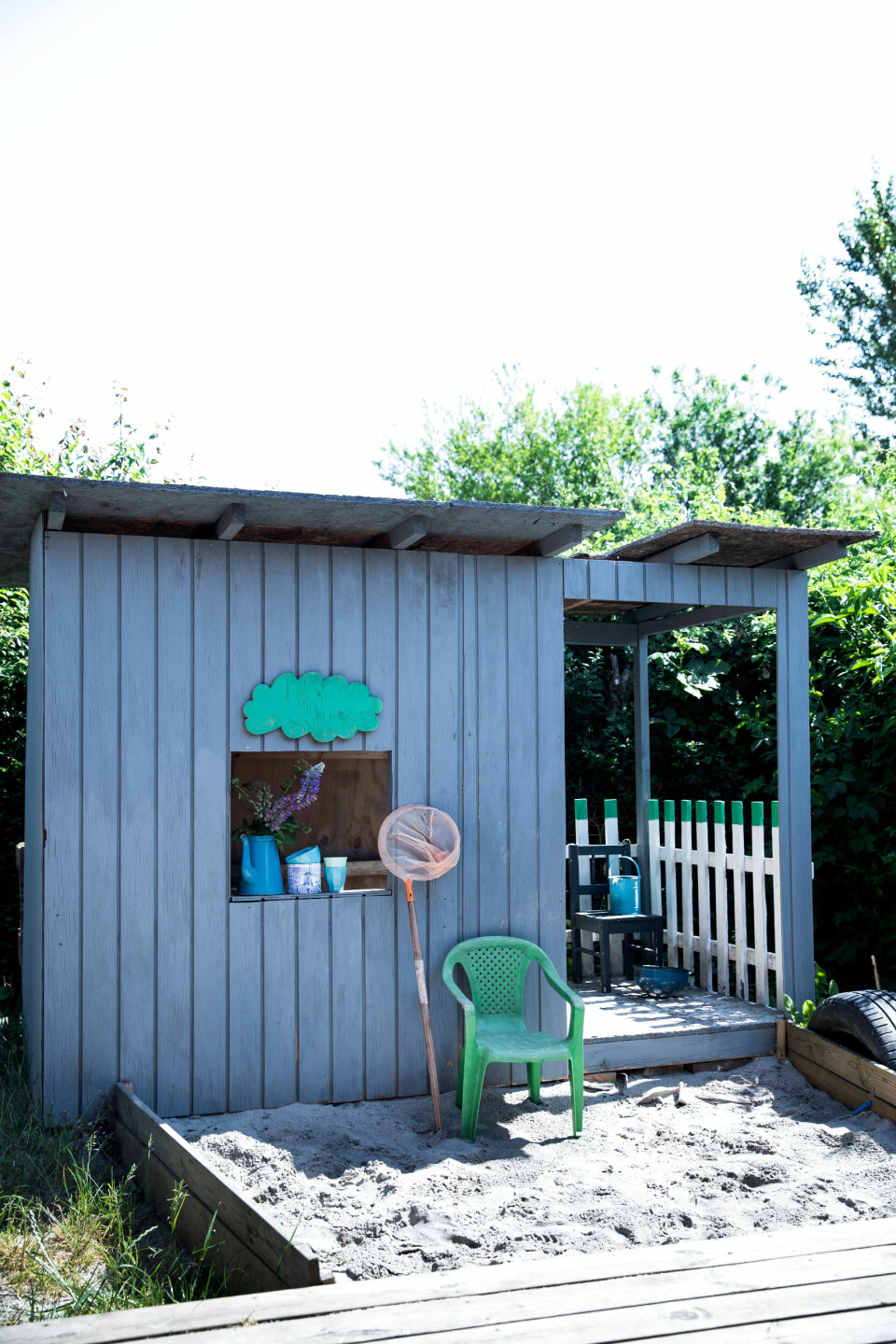 Herdis har bygget huset så højt, åbent og simpelt som muligt. Farven er hjemmerørt af maling, hun havde til overs, og skyen og toppen af stakittet er spraymalet grønt. Mellem legehuset og terrassen har Herdis lavet en sandkasse af overskydende terrassebrædder. Næste projekt er at få fat i noget tagpap til taget.
