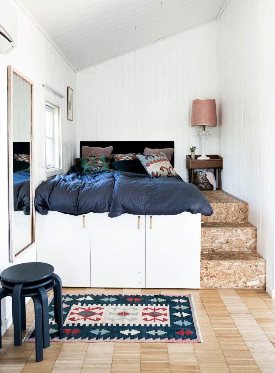 Sengen er bygget op på tre køkkenskabe fra Ikea, fundet på dba.dk, og på de OSB-plader, som parret havde til overs, da de istandsatte kolonihavehuset. Gulvtæppet har Martin fundet på et marked i Tyrkiet og sengetøjet er fra Føtex. Sengegavlen har Herdis selv lavet af en tynd plade, som hun har pakket ind i en tynd dyne og betrukket med møbelvelour. Natbordet fulgte med kolonihaven, da de overtog den.