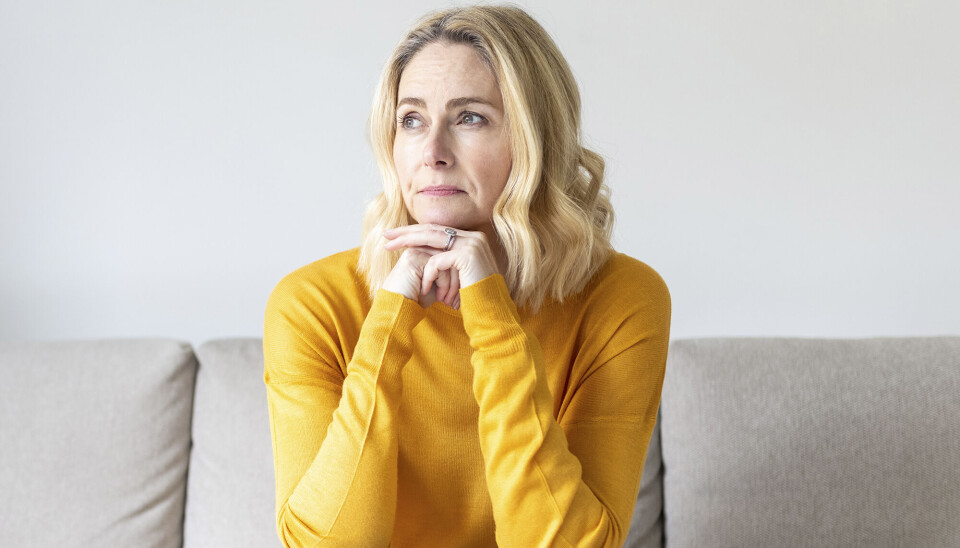 En kvinde, med en gul trøje, sidder på en sofa, og tænker.