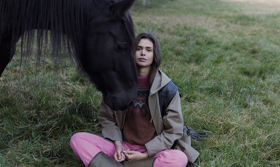 Amalie Reedtz-Thott sidder på græsset i skrædderstilling med kinden hvilende på hesten, Copaibas, mule hvilende på sin kind