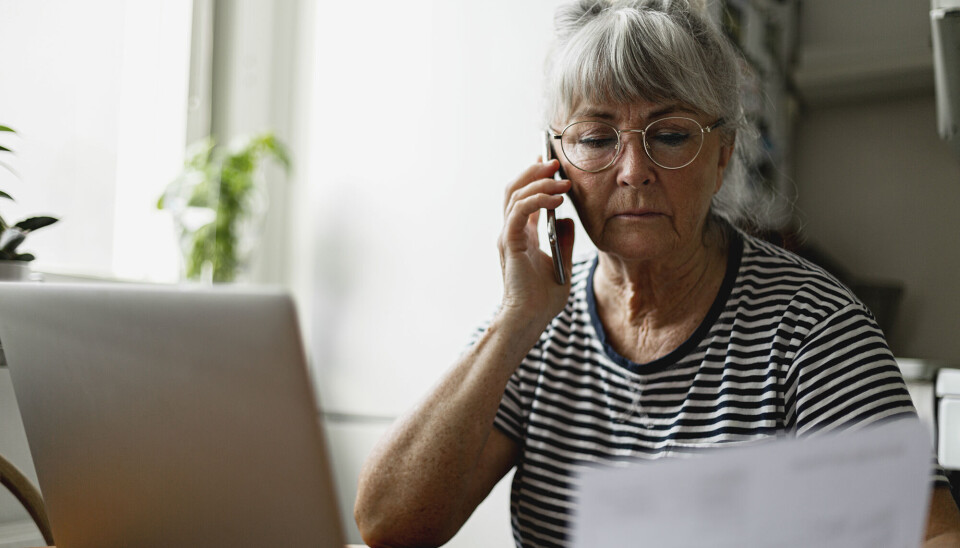 En ældre kvinde sidder foran sin computer, og taler i telefon.