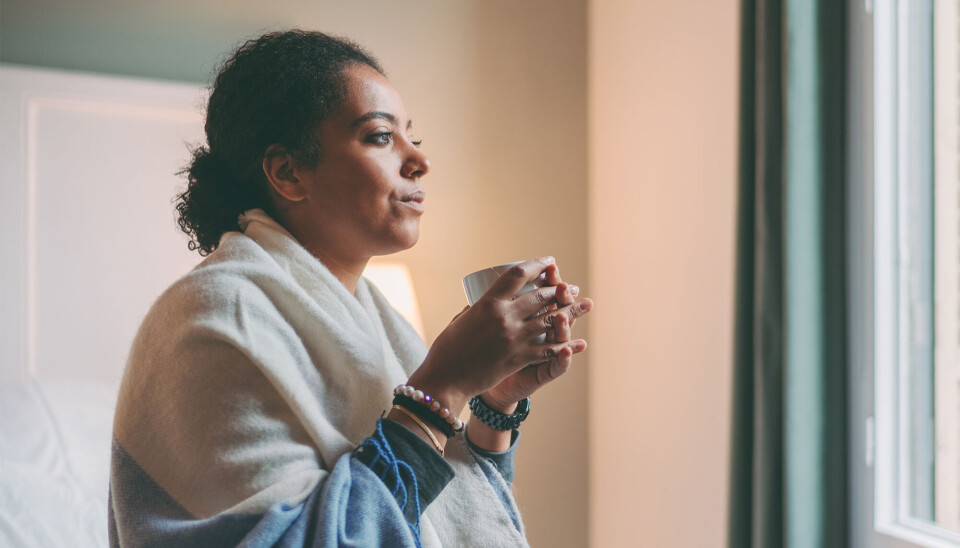 Kvinde sidder og drikker kaffe og kigger bekymret ud af vinduet