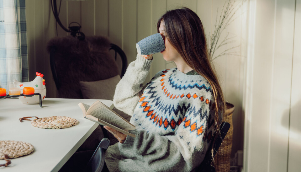 Billede 1 - Kvinde i grå sweater drikker te og læser i en bog