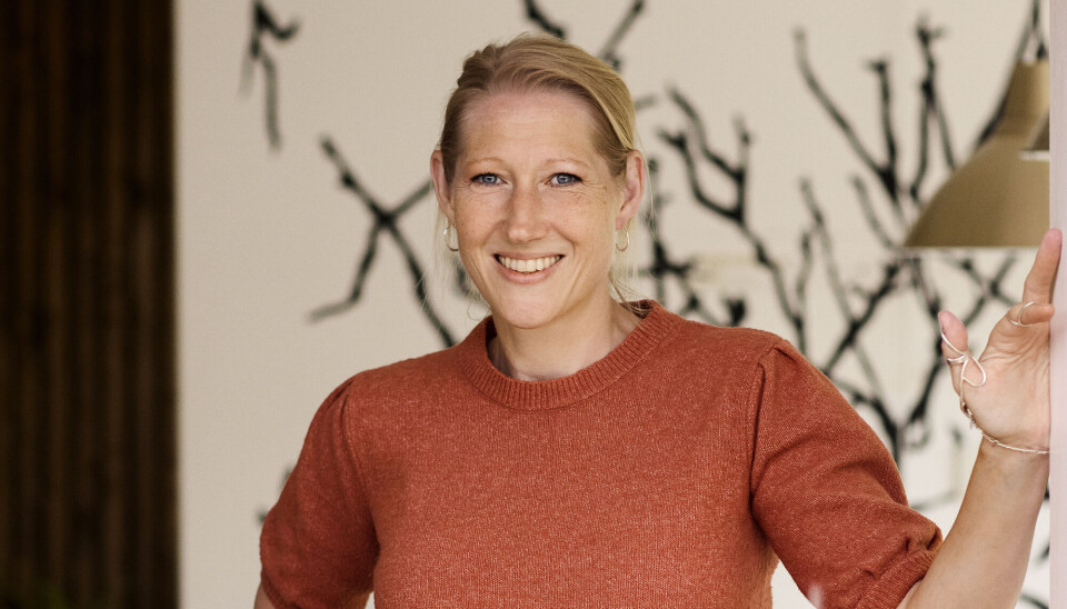Portræt af Karina Dahl-Olsen. Hun har en rustrød strikket t-shirt på. Hun har blondt hår, og guldøreringe på.