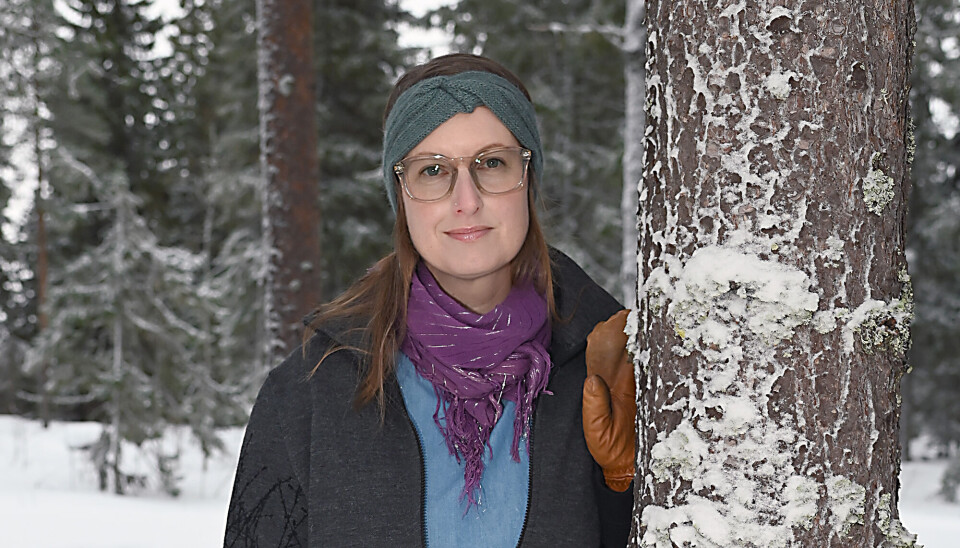 Portræt af Marie H. Lundh. Hun står udenfor, og der er sne. Hun læner sig op ad en træstamme. Hun har et grønt pandebånd på, et lilla tørklæde og cognac-farvede handsker på. Hun har en lyseblå trøje på, og en mørkeblå jakke på, som er åben.