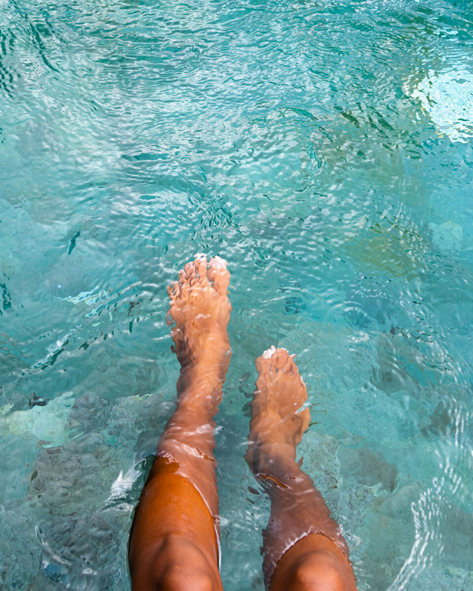 En kvinde sidder og dypper sine ben i en pool. Vi ser kun benene og vandet.