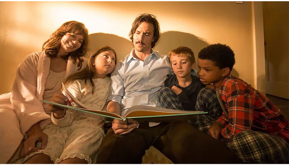 Familien Pearson fra serien 'This Is Us'. De sidder en mand, kvinde, og tre børn. De sidder og kigger i en bog, og børnene, samt moderen, har nattøj på.