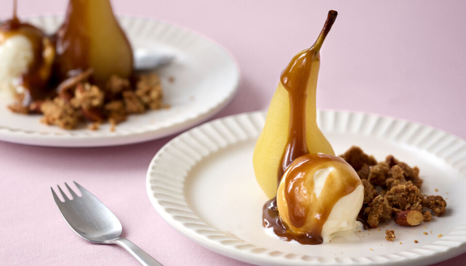 Porcherede pærer med butterscotch, crumble og vaniljeis. Serveret på hvide tallerkner, der står på en lyserød dug.