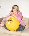 Caroline Albertine Minor sidder på en beige sofa. Hun har en lyserød jakke på, og sidder ned en stor bold, man kan hoppe på, som forestiller en giraf.