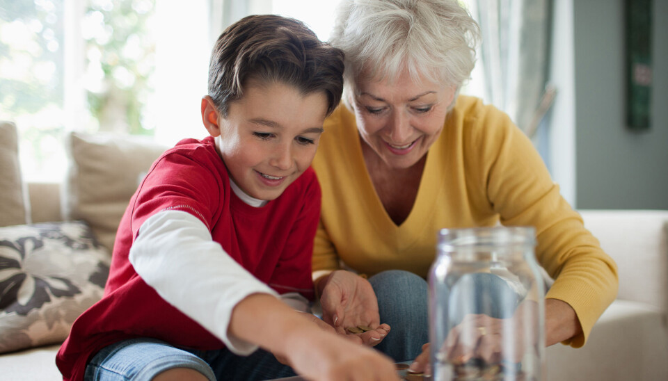 En dreng sidder med sin bedstemor. Han har en hvid langærmet t-shirt på, og en rød t-shirt udenpå. Hun har en gul langærmet trøje på. De ser glade ud.