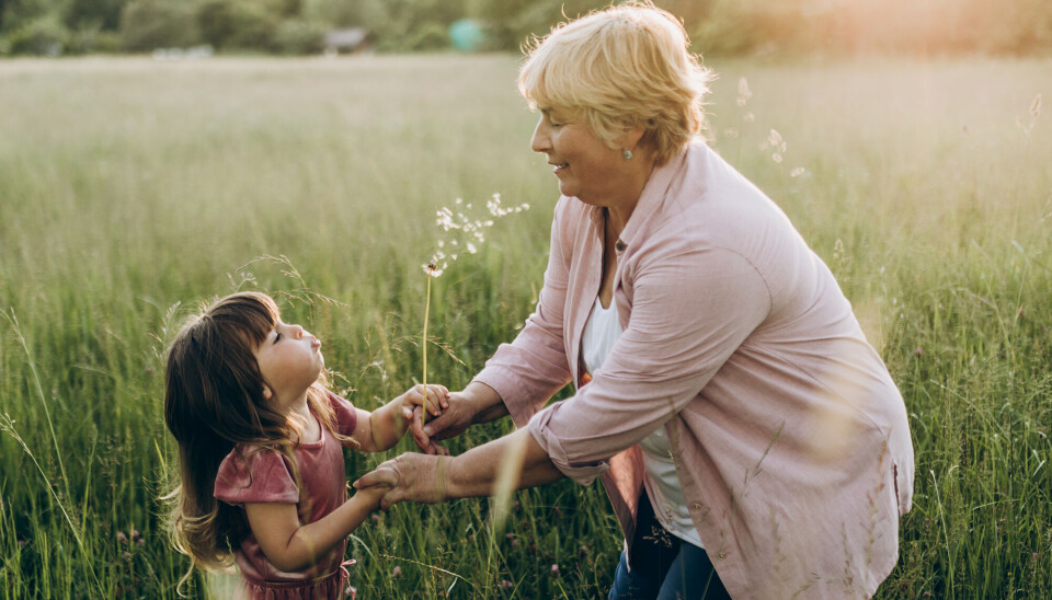 En bedstemor med sit barnebarn. De står ude på en græsmark, og de holder hinanden i hænderne.