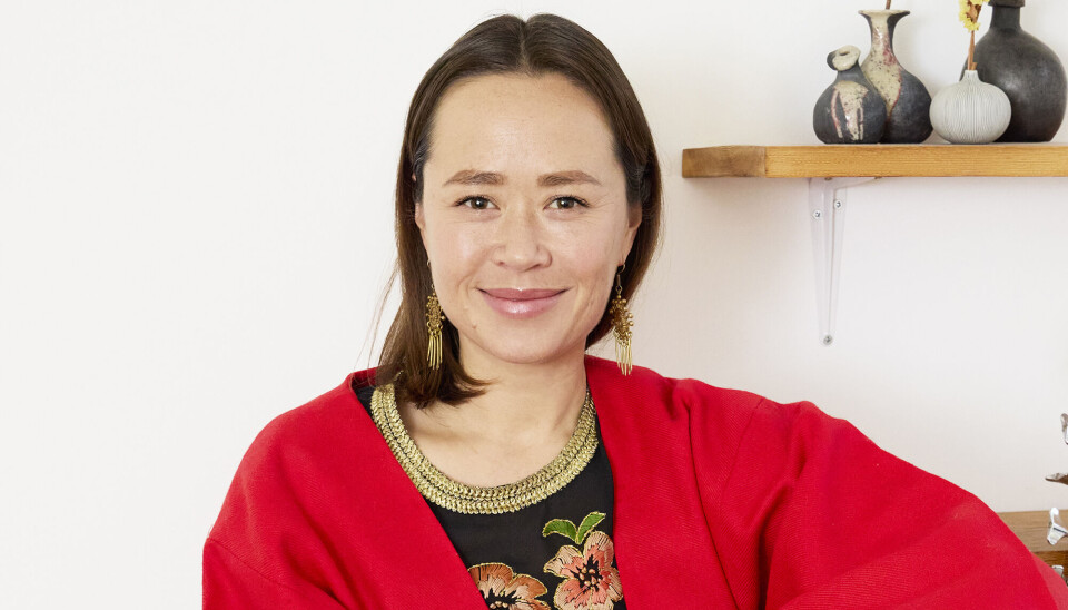 Portræt af Ida Kudo. Hun smiler, og hun har hængeøreringe i. Hun har en rød kimono på, og en blomstret bluse indenunder.