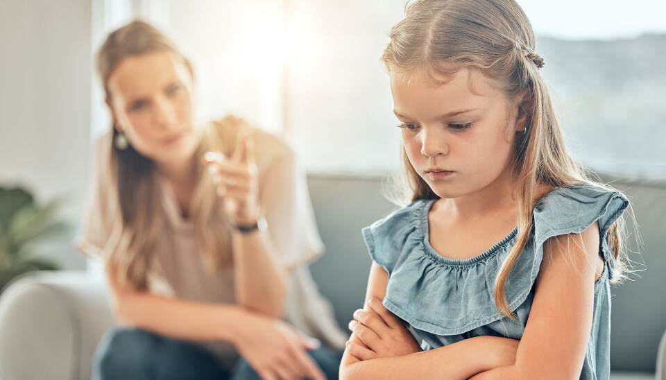 Lille pige står i forgrunden med krydsede arme. Hun kigger nedad og ser utilfreds ud. I baggrunden ses en kvinde - sandsynligvis hendes mor - som har en løftet pegefinger.