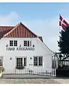 Et billede af Fanø Krogaard. Huset er hvidt, med et rødt tag. I baggrunden flager Dannebrog,