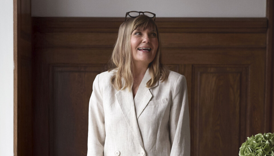 Portræt af Anette Kristine Poulsen. Hun har en hvid blazer på, og briller sat op i håret.