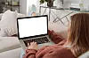 Close-up Casual freelance young woman in modern living room sitting on a sofa with legs crossed watching laptop in white screen while relaxing on the sofa at home