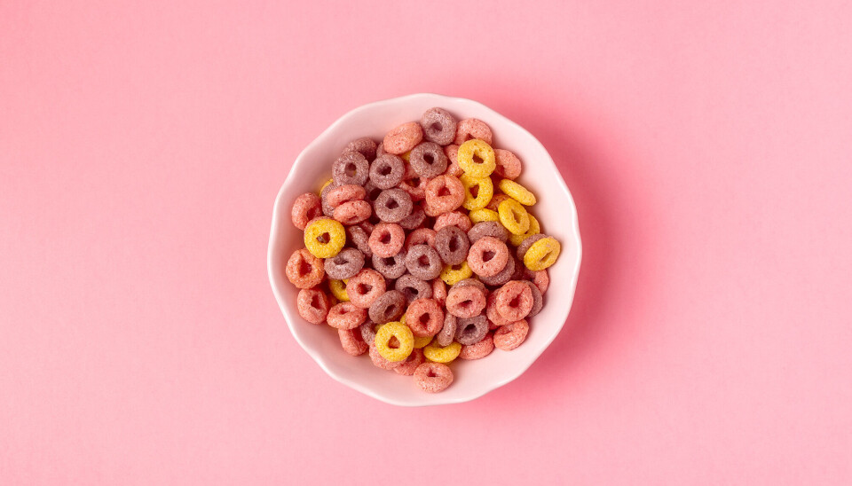 Et billede af farverige cereals. De ligger i en hvid skål, og står på en lyserød overflade.