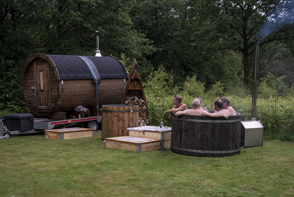 Billedet viser en flok mænd, der sidder i et vildmarksbad. Til venstre for dem står en sauna og et koldtvandskar.