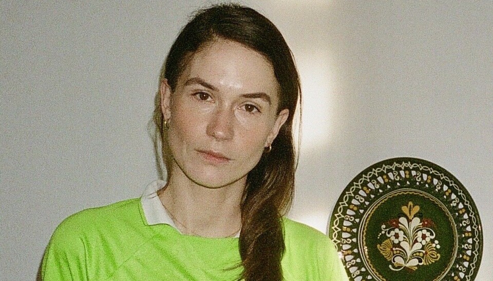 Forfatter Emma Rosenzweig i neongrøn sportstrøje og nederdel står tilbagelænet op ad et bord.