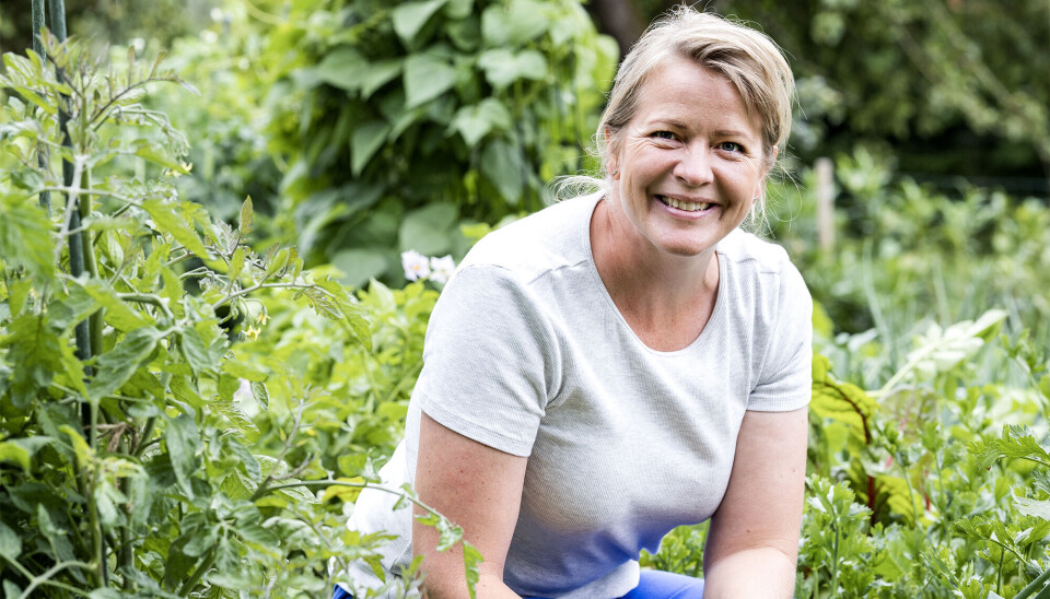 Foto af Kristina Winther. Hun har en grå t-shirt på. Hun sidder i sin have, og er omgivet af en masse planter.