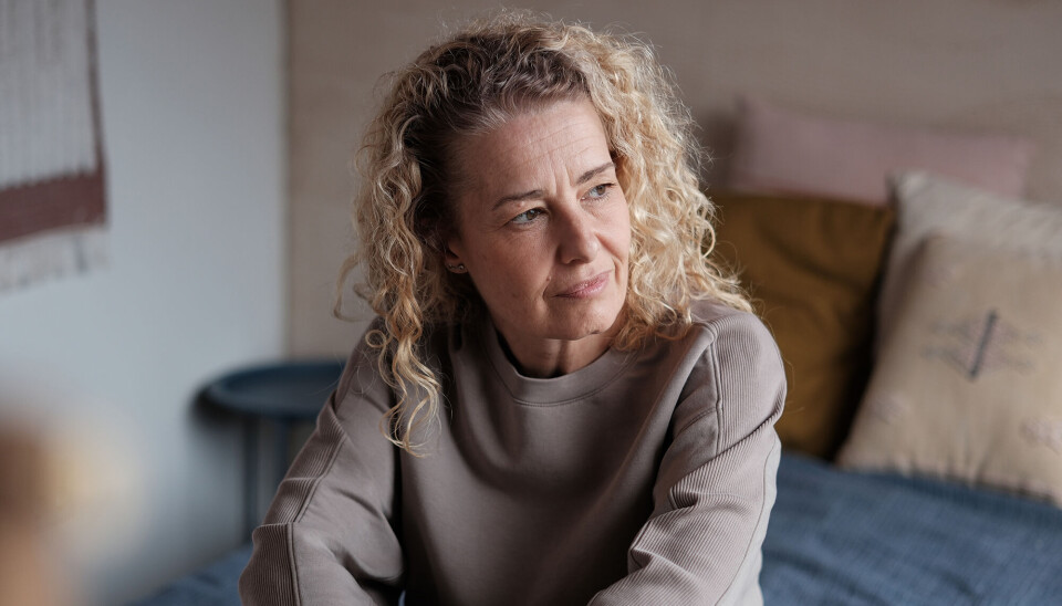 En kvinde i midt 50'erne. Hun ser fortvivlet ud. Hun har krøllet hår, og en grålig sweater på.