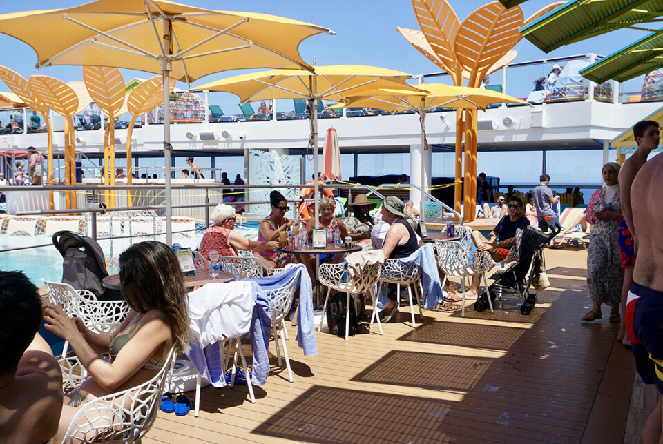Billede af cruisegæster, der sidder under gule parasoller ved en af de to pools på skibet.