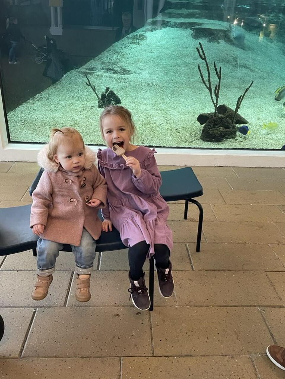 Johanne og Asta med farmor i Kattegatcentret. De to børn sidder på en bænk.