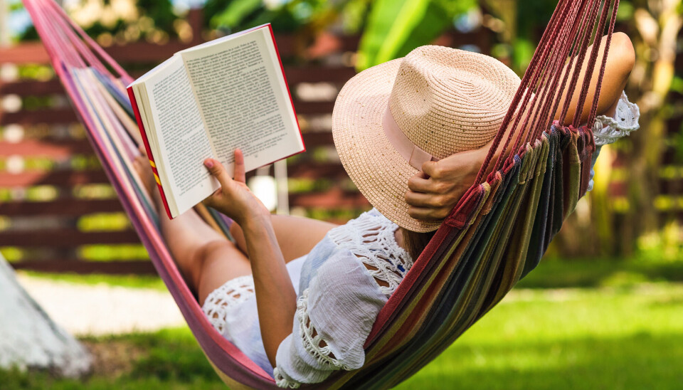 En kvinde ligger i en hængekøje og læser. Hun har en hat på og en hvid kjole.