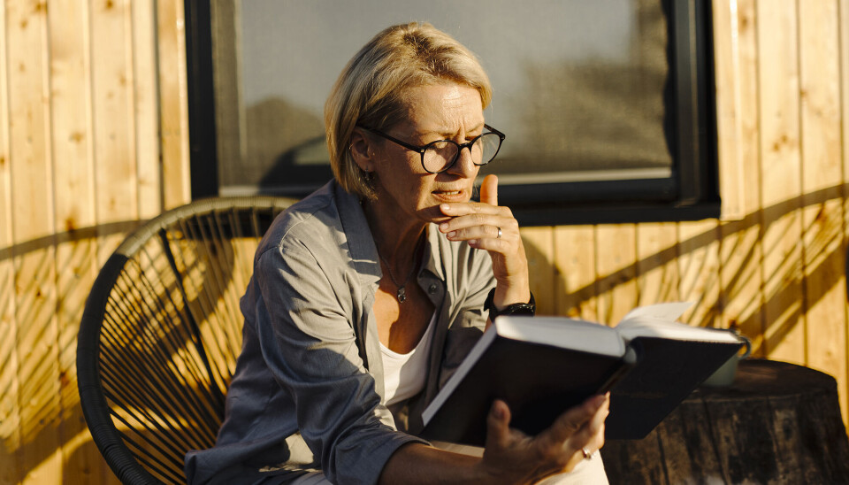 En kvinde sidder i en rund, flettet stol. Hun sidder udenfor i solnedgangen, og læser i en bog.