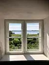 Billede taget ud igennem et hvidt vindue i Malergården. Igennem vinduet kan man se et stort, grønt område, og i horisoten er vandet.