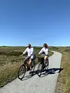 To personer cykler på en grussti. Himlen er blå, og de er begge iført hvide skjorter og shorts.