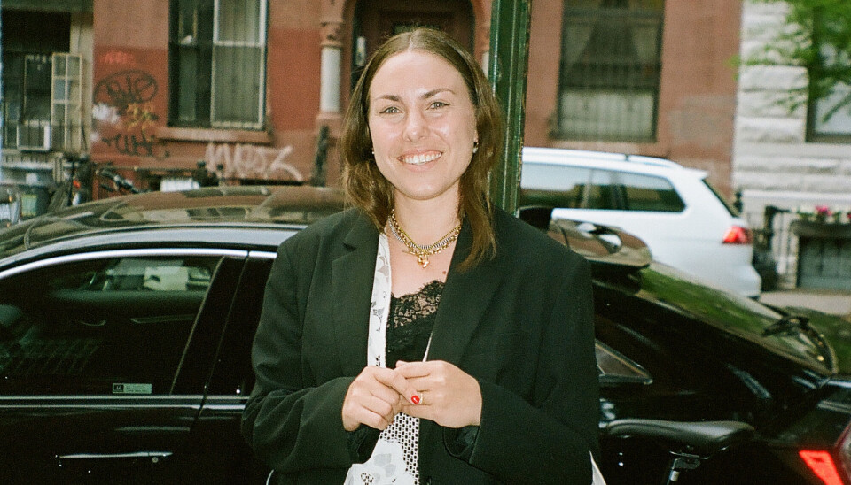 Foto af Rebecca Francker. Hun har en sort blazer på, og en kjole med hvide blonder. Hun står ude på en gade, og bag hende er en sort bil.