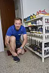 Niels Mose, der er i færd med at binde sine løbesko. Bag ham står en skoreol med en række forskellige løbesko i forskellige farver på.