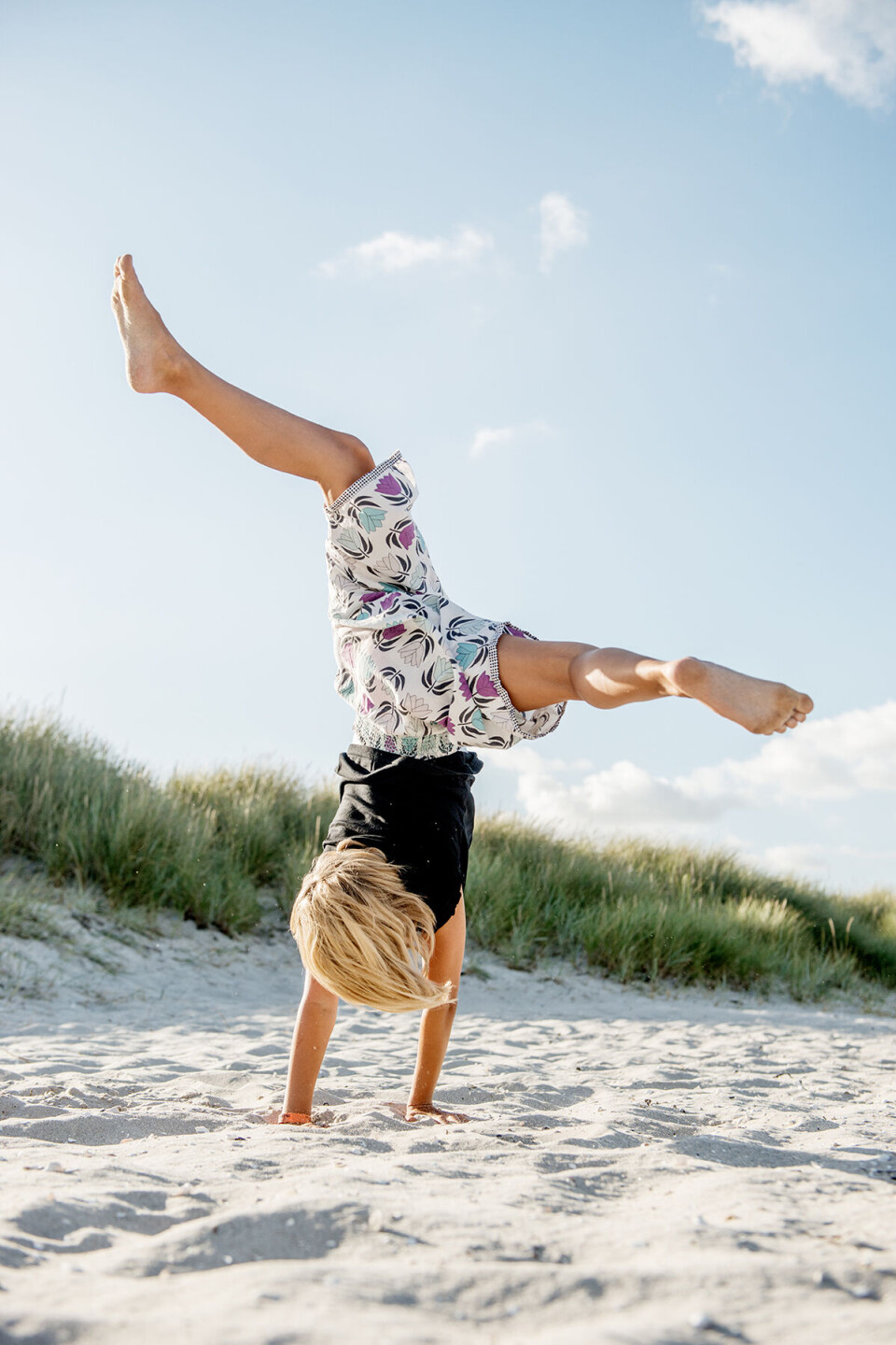 Dreng med lyst hår, der står på hænder på stranden.