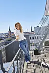 Sofie Lassen-Kahlke står på en tagterasse - man kan se bygninger i baggrunden. Hun ses i fuld figur iført hvid bluse, jeans og hvide sneakers. Hun læner sig op ad rækværket.