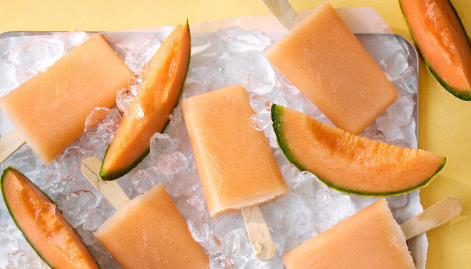 Et billede af ispinde, der er lavet af cantaloupmelon. De ligger på et fad med isterninger, og der er også skiver af cantaloupmelon.